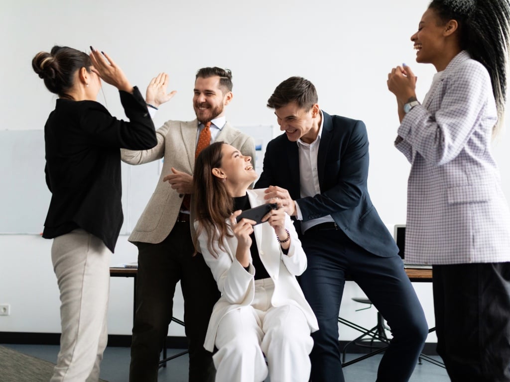 Equipo de colaboradores sonriendo y compartiendo en la oficina, representando la transformación cultural en las empresas y un ambiente de trabajo colaborativo.