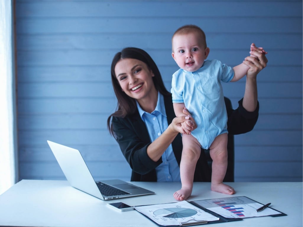 Mujer profesional trabajando con su bebé en brazos en la oficina, representando el reconocimiento a madres colaboradoras en el Día de la Madre en empresas.