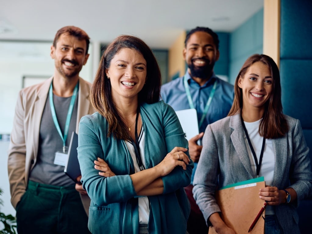 Equipo de trabajo multicultural sonriendo en la oficina, reflejando compromiso laboral, colaboración y motivación en el entorno empresarial.