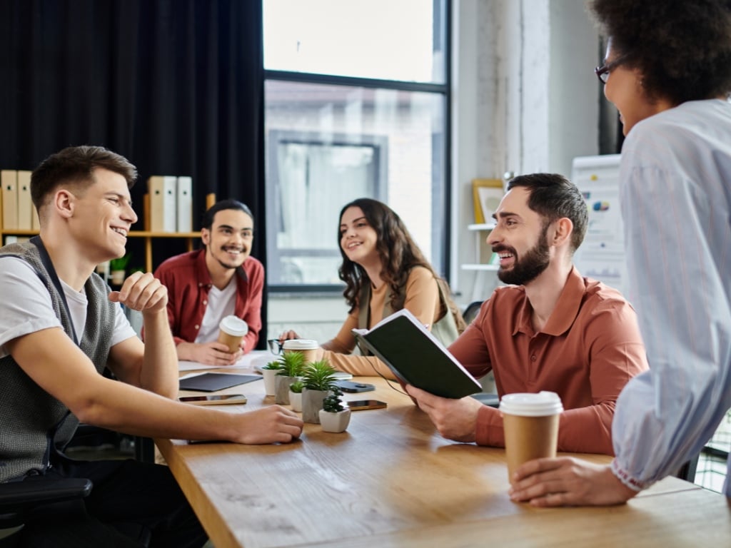 Equipo de trabajo conversando en reunión mientras un líder escucha activamente, reflejando un clima laboral positivo y comunicación efectiva.