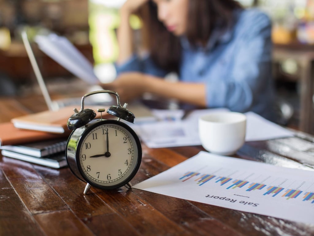 Mujer revisando documentos y el tiempo de trabajo en su escritorio, concepto de jornada laboral en España.