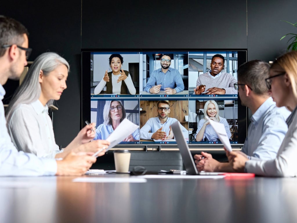 Equipo corporativo participando en videollamada global en sala de reuniones, representando tendencias de trabajo híbrido y transformación digital en las organizaciones.