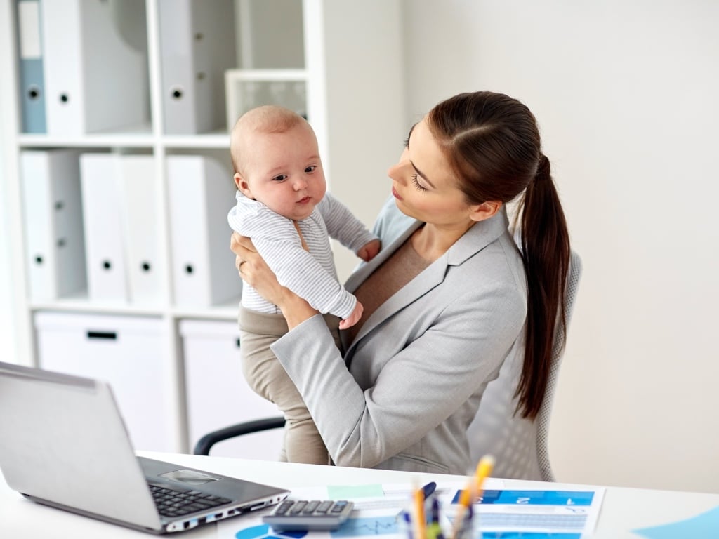 Madre trabajadora con su bebé usando laptop en la oficina, representando el reconocimiento a madres trabajadoras en empresas